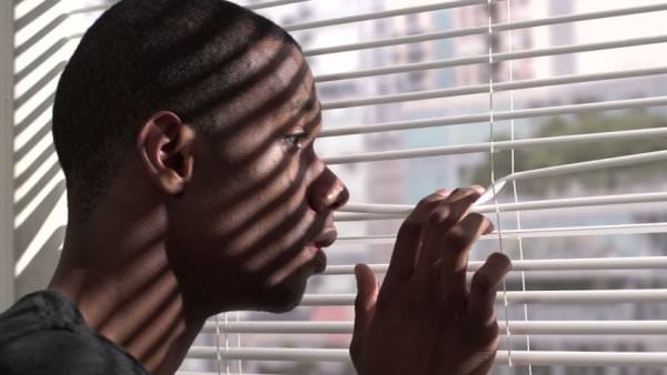 There are many differing stereotypes about addiction. Between the color of his skin and the paranoid way he’s peering through the blinds, this young man fits the bill for at least two of them. Read on to discover why this image is unfair. (Burlingham/Shutterstock)
